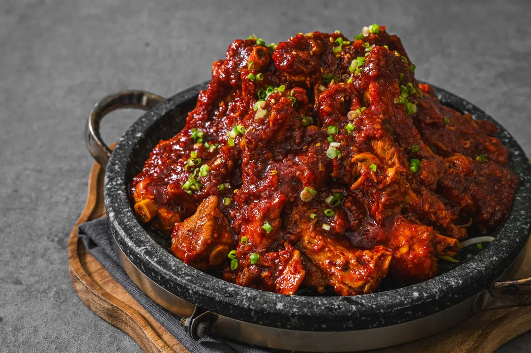 돌판 위에 수북이 쌓인 붉은 양념 등갈비구이와 송송 썬 파 클로즈업
