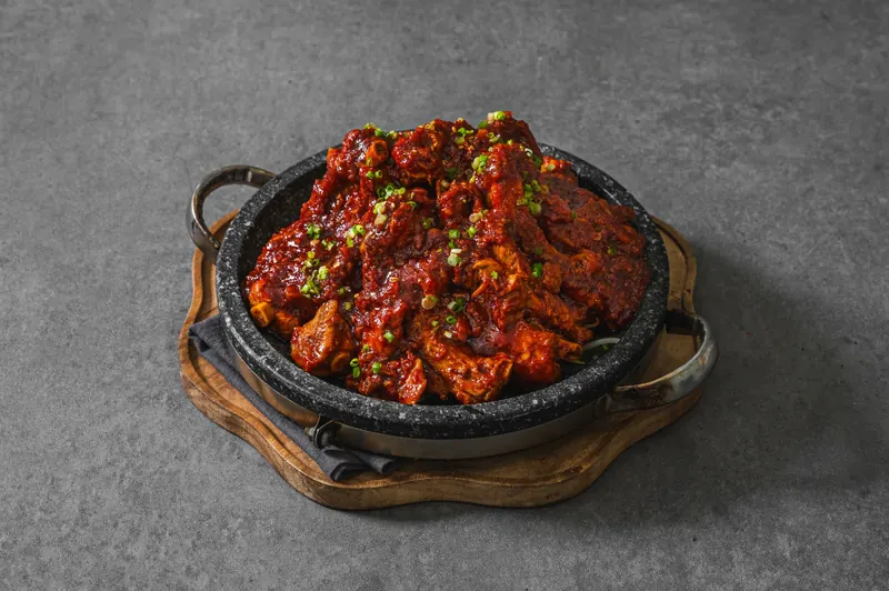 넓은 돌판에 담긴 양념 등갈비구이와 파 고명
