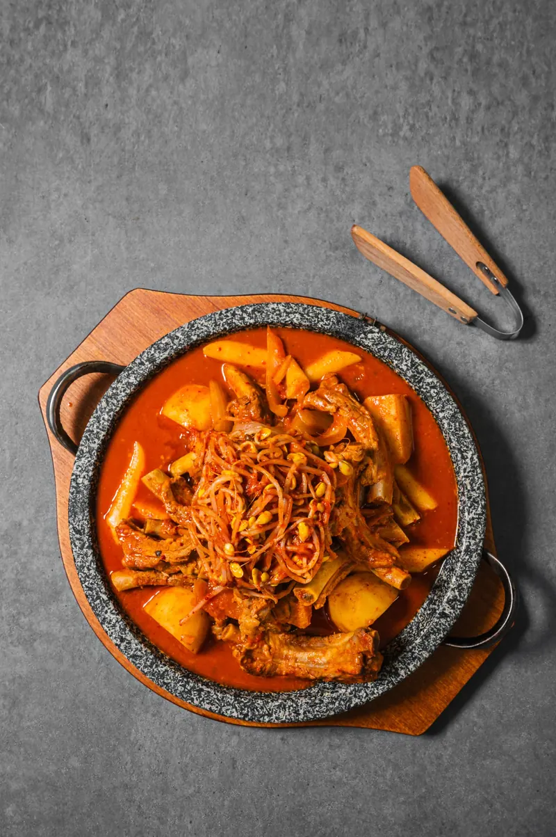 세로 구도의 돌판 김치 등갈비찜과 집게