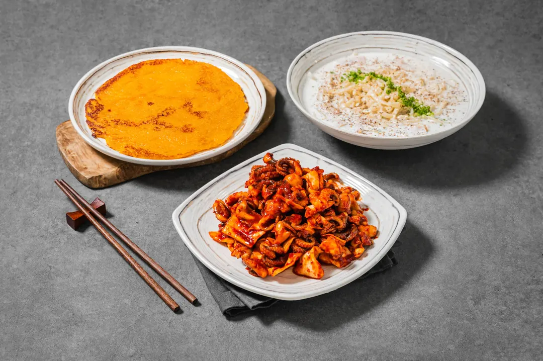 둥근 부침 요리와 하얀 국수 그릇, 쭈꾸미볶음이 함께 놓인 식사 한상