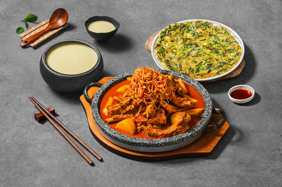 막걸리, 부쭈전, 김치 등갈비찜과 젓가락이 놓인 회색 테이블 상차림